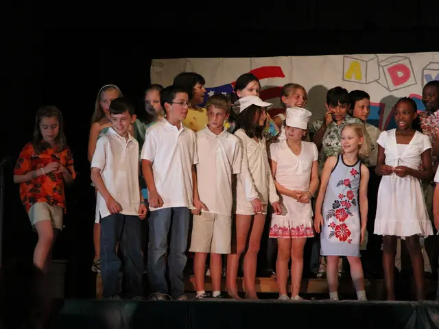 In this image few kids are standing on the stage. Middle of the image two kids are wearing caps....