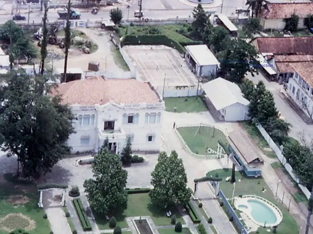 In this image we can see the top view of the buildings, trees, vehicles, plants, grass, pool and...